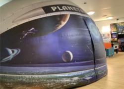 A portable planetarium dome with space-themed graphics. The dome is inflatable and has images of planets, a spacecraft, and stars on its exterior, with the word 