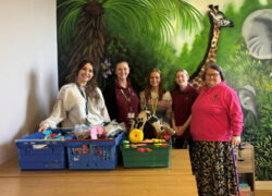 A group of staff standing behind tables displaying crates of donated pet supplies, including toys, blankets and food, in front of a colourful wildlife mural.