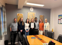 Staff at Cygnet Nield House gathered together in a meeting room, celebrating the service receiving Triangle of Care accreditation for working in partnership with carers.