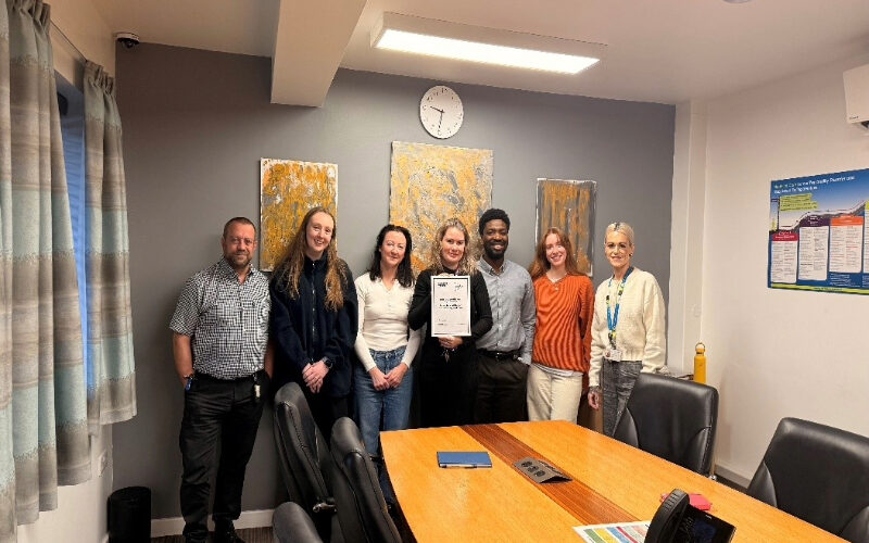 Staff at Cygnet Nield House gathered together in a meeting room, celebrating the service receiving Triangle of Care accreditation for working in partnership with carers.