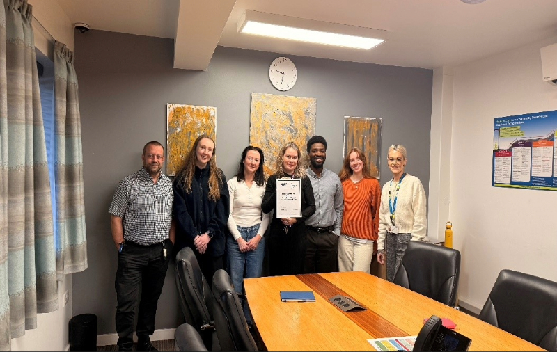 Staff at Cygnet Nield House gathered together in a meeting room, celebrating the service receiving Triangle of Care accreditation for working in partnership with carers.
