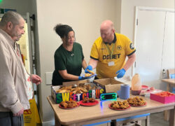 Several people stand around a table serving and selecting food from an Eid buffet.