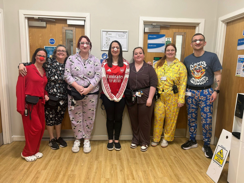 The Spencer Ward team standing together and smiling in a corridor at Cygnet Hospital Sheffield, dressed in pyjamas for a Comic Relief fundraiser. They are wearing a mix of patterned and colourful outfits, including Nightmare Before Christmas pyjamas, a set with rubber ducks and an Arsenal shirt.