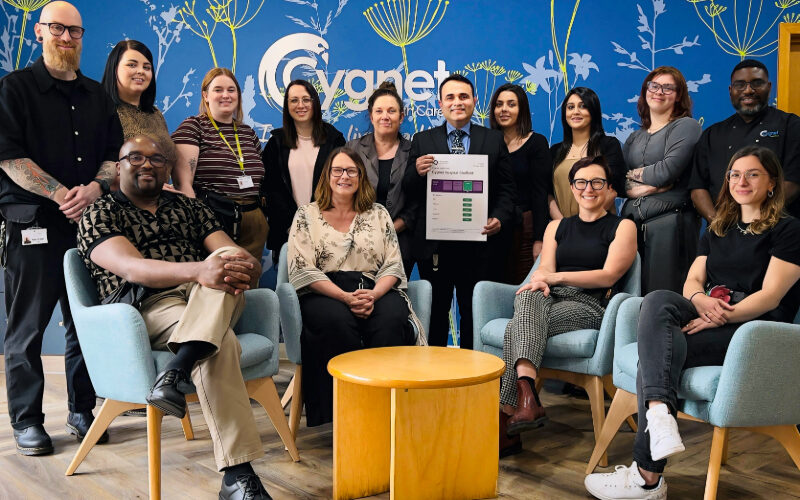 The Cygnet Hospital Sheffield team pose in the reception celebrating their recent CQC success. A man in the middle of the group holds a printout of the results.