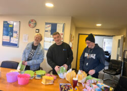 Three people standing around a table at Cygnet Sherwood House, smiling while taking part in Easter arts and crafts.