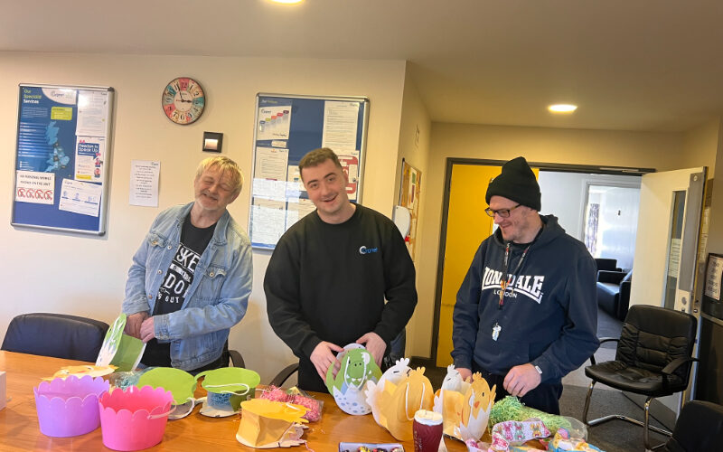Three people standing around a table at Cygnet Sherwood House, smiling while taking part in Easter arts and crafts.