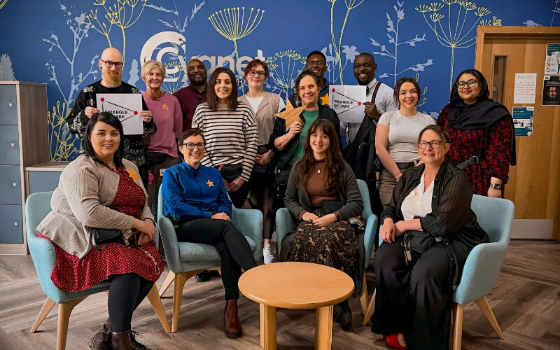 The Cygnet Hospital Sheffield team smiling to celebrate the retention of the Triangle of Care in the reception holding stars and the accreditation logo
