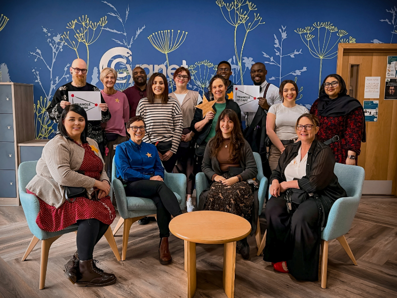 The Cygnet Hospital Sheffield team smiling to celebrate the retention of the Triangle of Care in the reception holding stars and the accreditation logo