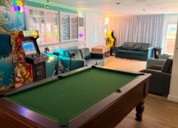 The social hub at Cygnet Lodge Lewisham from the doorway, including pool table, seating areas, arcade machine and exercise bike in soft lighting