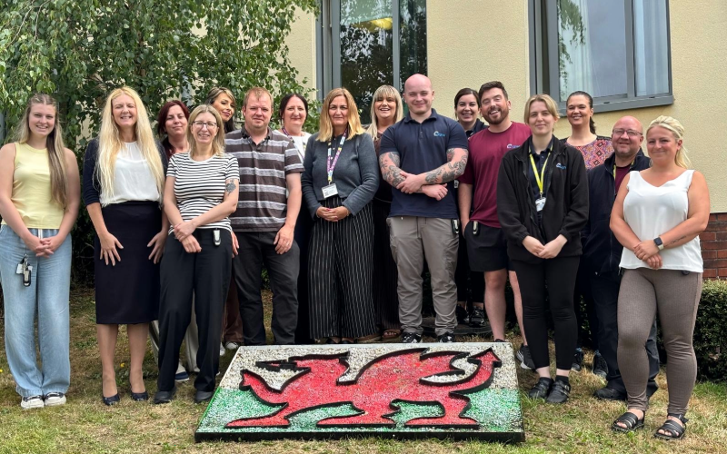 The team stood outside Cygnet Delfryn Lodge with a Welsh flag made of stones on the floor at their feet
